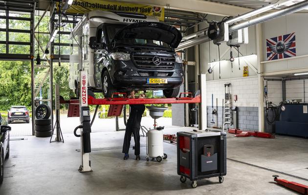 Camper op de brug in de garage met daaronder een monteur